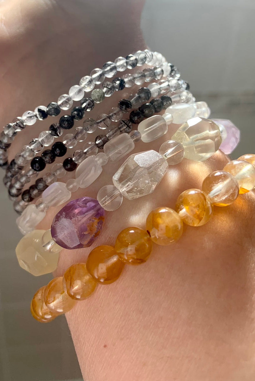 Crystal bracelet stack featuring Golden Healer Quartz, faceted amethyst + quartz, white moonstone, and black tourmaline in quartz
