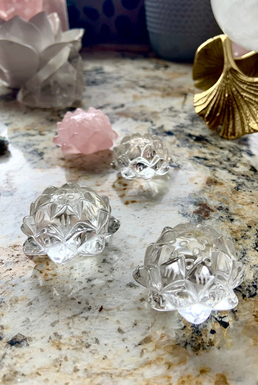 Carved clear quartz crystal lotus flowers displayed on a surface with other crystals.