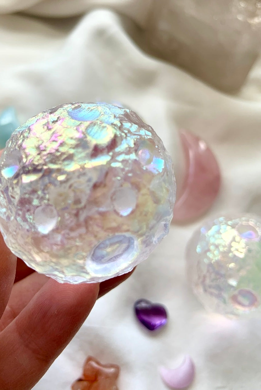 Close-up of Angel Aura Full Moon sphere with soft crystal background on white silk — glowing lunar texture with ethereal rainbow sheen.