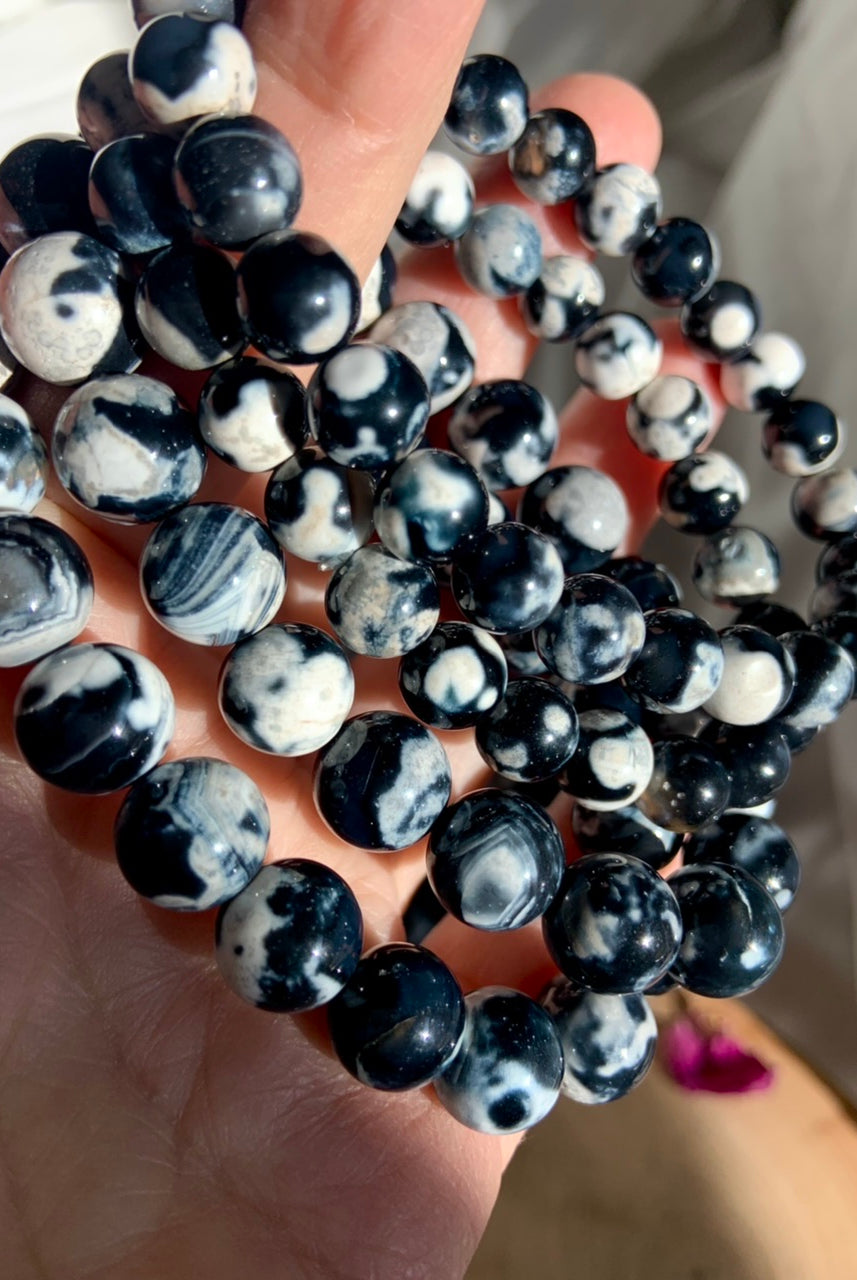 Closeup of stacked Orca Agate bracelets in assorted sizes, showing high polish and unique swirling patterns
