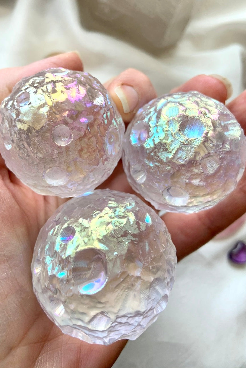 Three Angel Aura Quartz moon spheres shown in hand — iridescent crystal carvings for intuition, insight & spiritual connection.