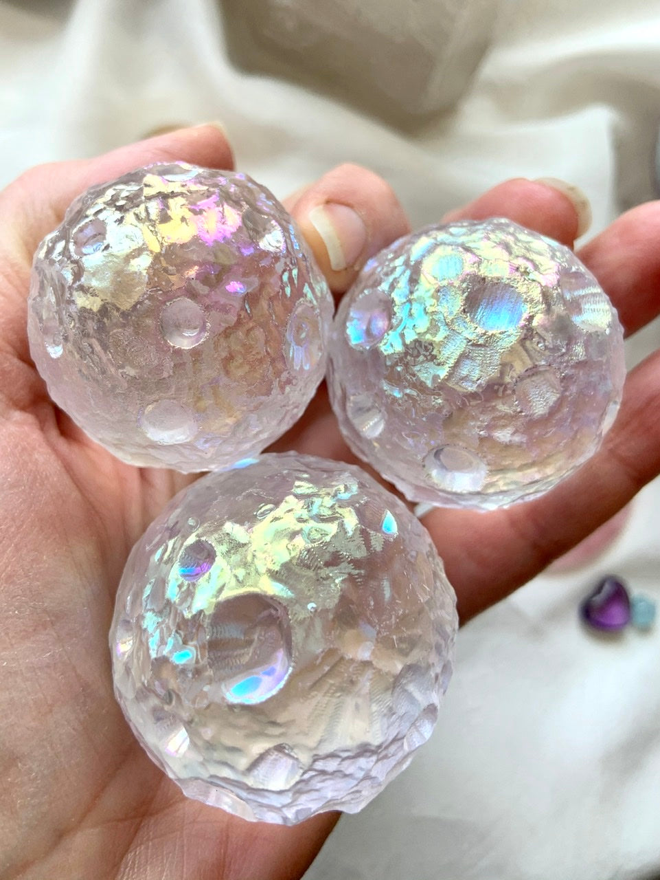 Three Angel Aura Quartz moon spheres shown in hand — iridescent crystal carvings for intuition, insight & spiritual connection.