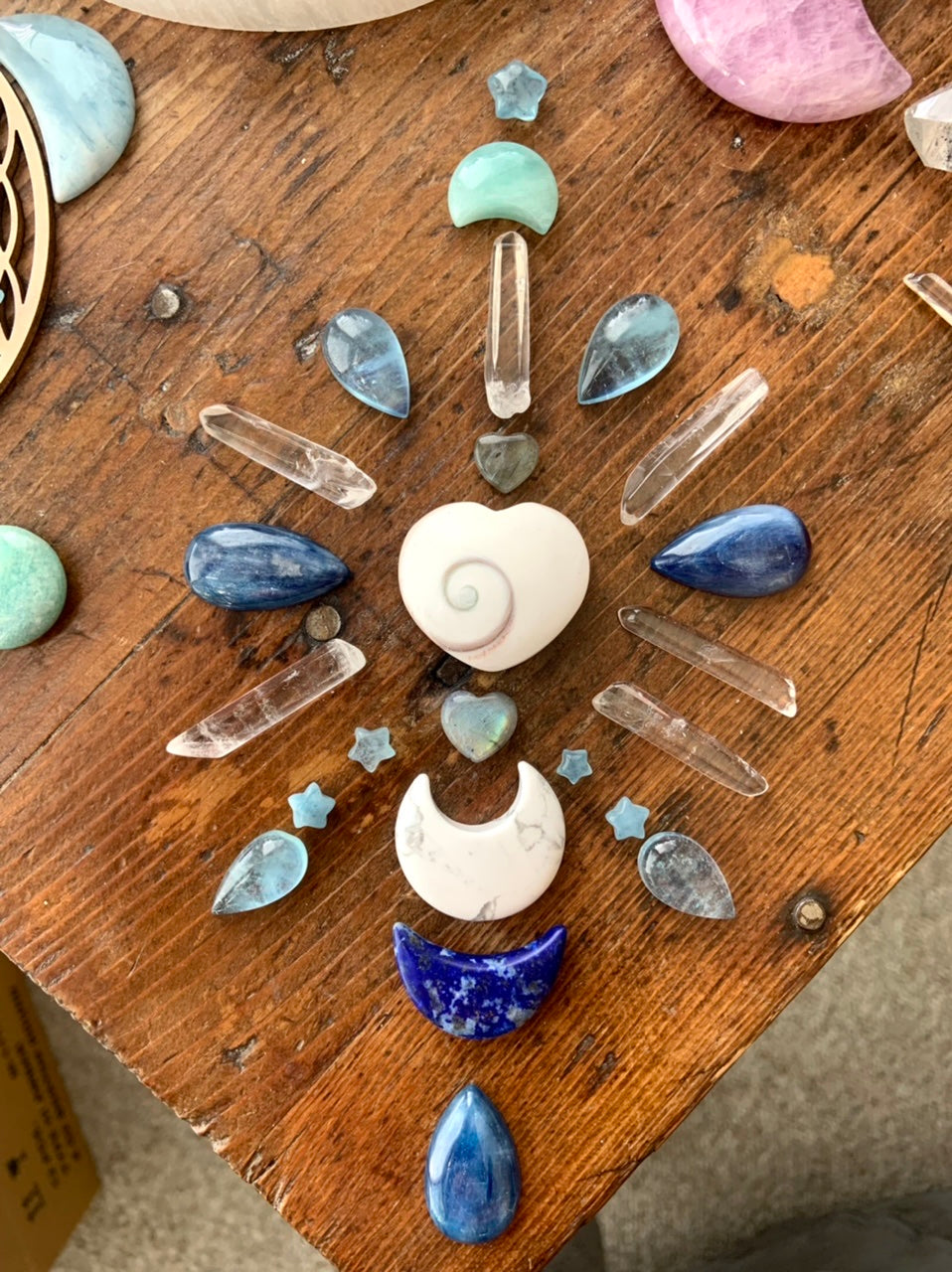 Small clear quartz crystal points arranged in chakra-inspired crystal grid on wooden table with moon carvings and sacred center stone