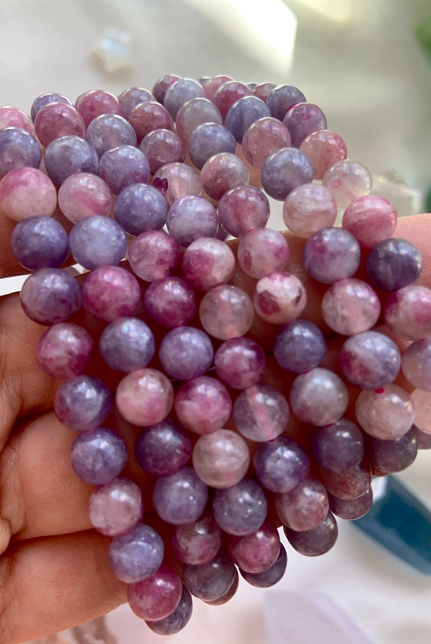Closeup of Unicorn Stone crystal bracelets held on a hand — high quality pink and purple beads with Pink Tourmaline in Lepidolite for heart chakra healing.
