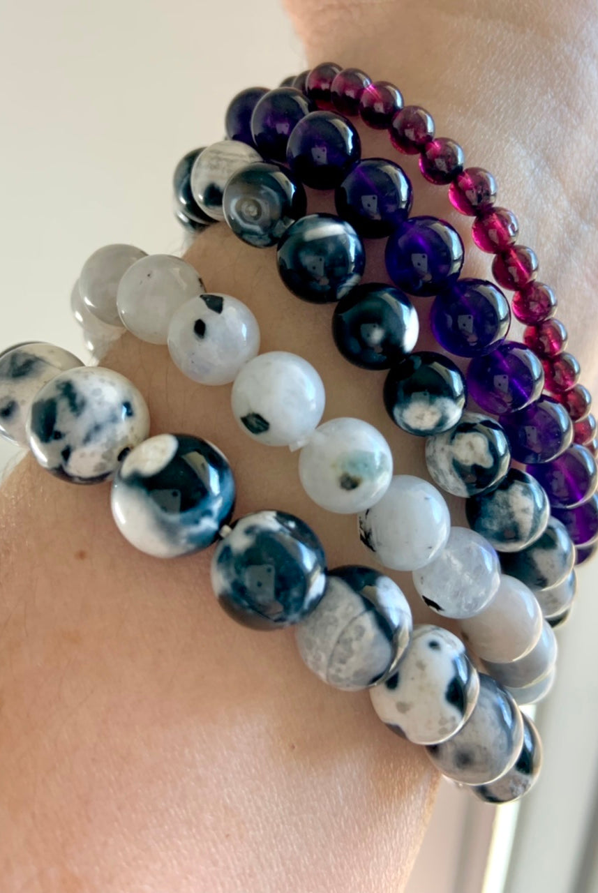 Stack of healing crystal bracelets featuring Orca Agate, Rainbow Moonstone, Amethyst, and Garnet for chakra alignment and emotional healing