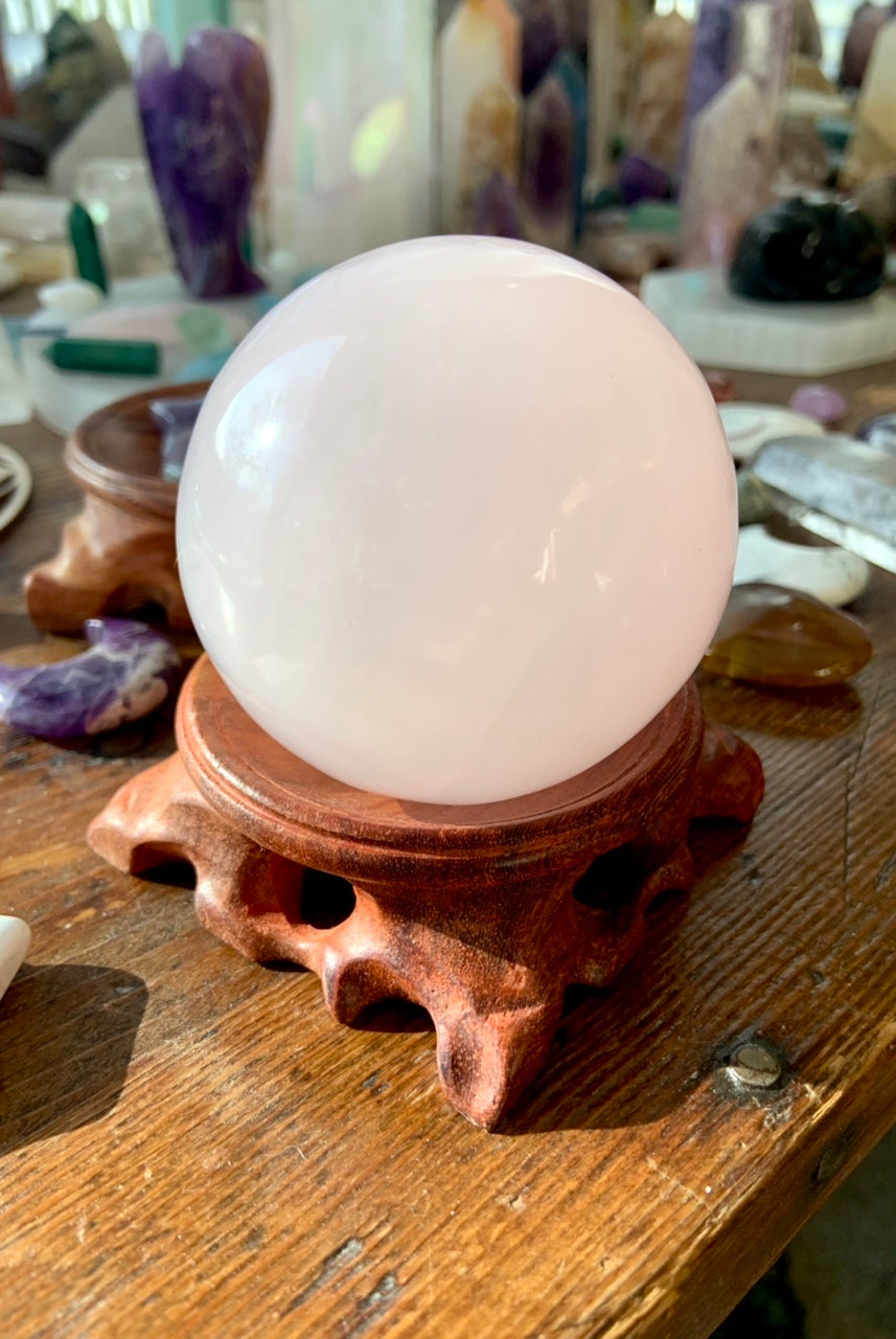 pink mangano calcite sphere on a wood stand