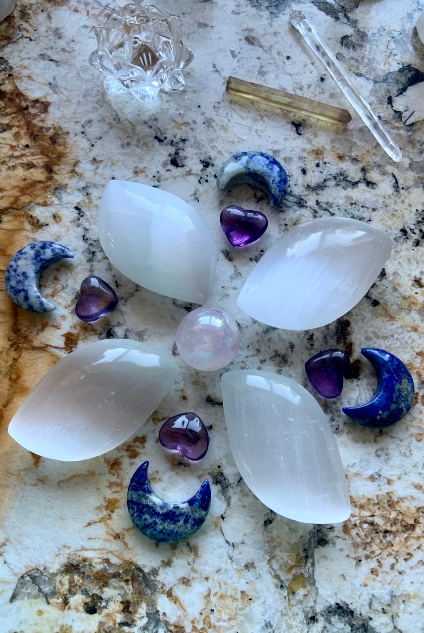 Flower-shaped crystal grid with selenite petals, Lapis Lazuli moons, and Aura Rose Quartz centerpiece — sacred layout for spiritual alignment