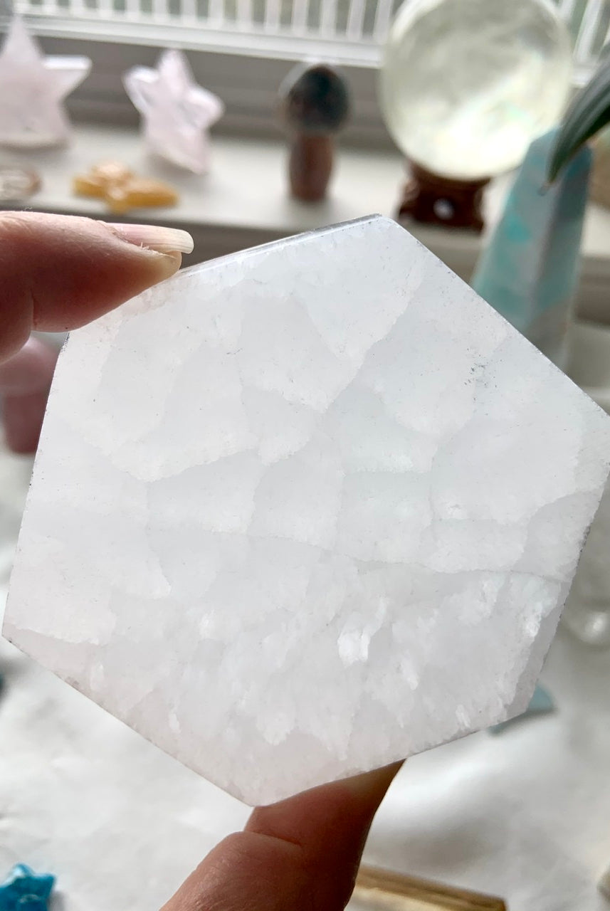 Closeup of a Selenite Hexagon Charging Plate held to the light, showing natural glow, translucence, & pattern in the stone