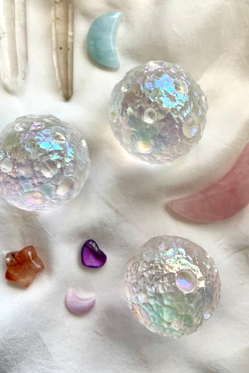 Angel Aura Full Moon crystal spheres arranged with cosmic crystals — rose quartz moon, aquamarine moon, quartz points — on soft white silk for dreamy display.