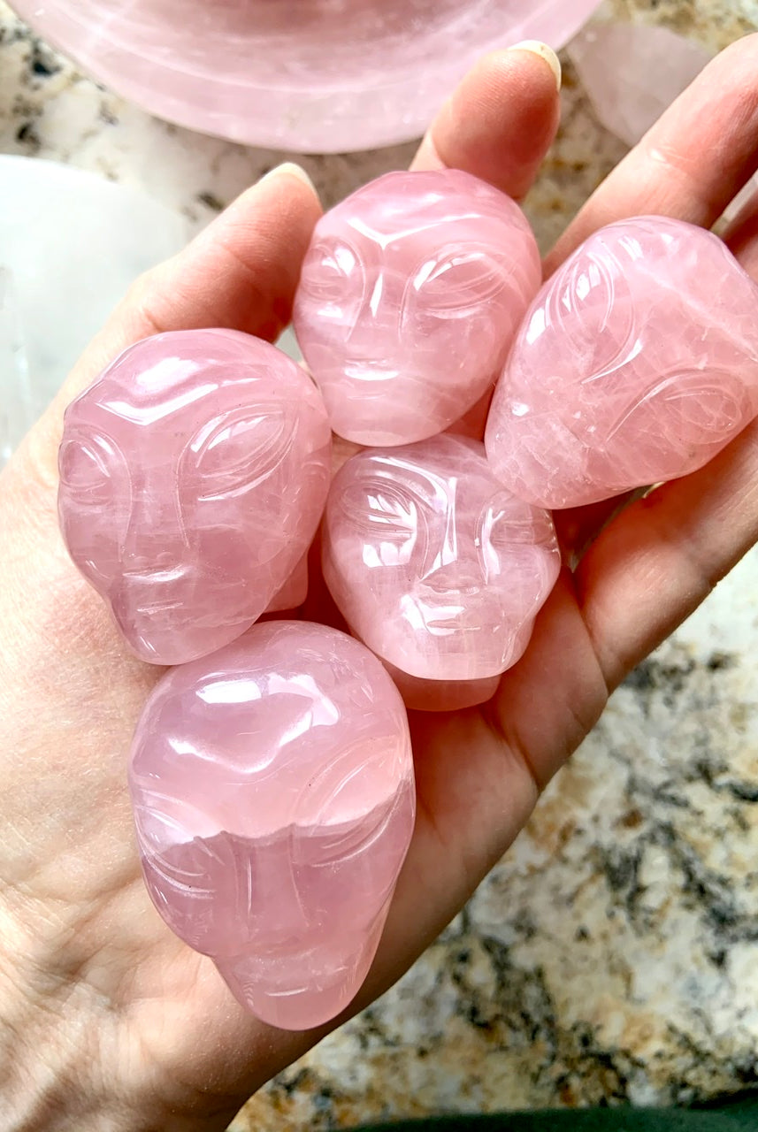 Group of five pink Rose Quartz alien face carvings with high polish, displayed on open palm