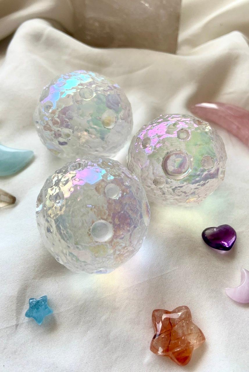 Angled shot of three Angel Aura Full Moon spheres with rose quartz moon, aquamarine moon & amethyst heart — cosmic crystal grid on white silk.