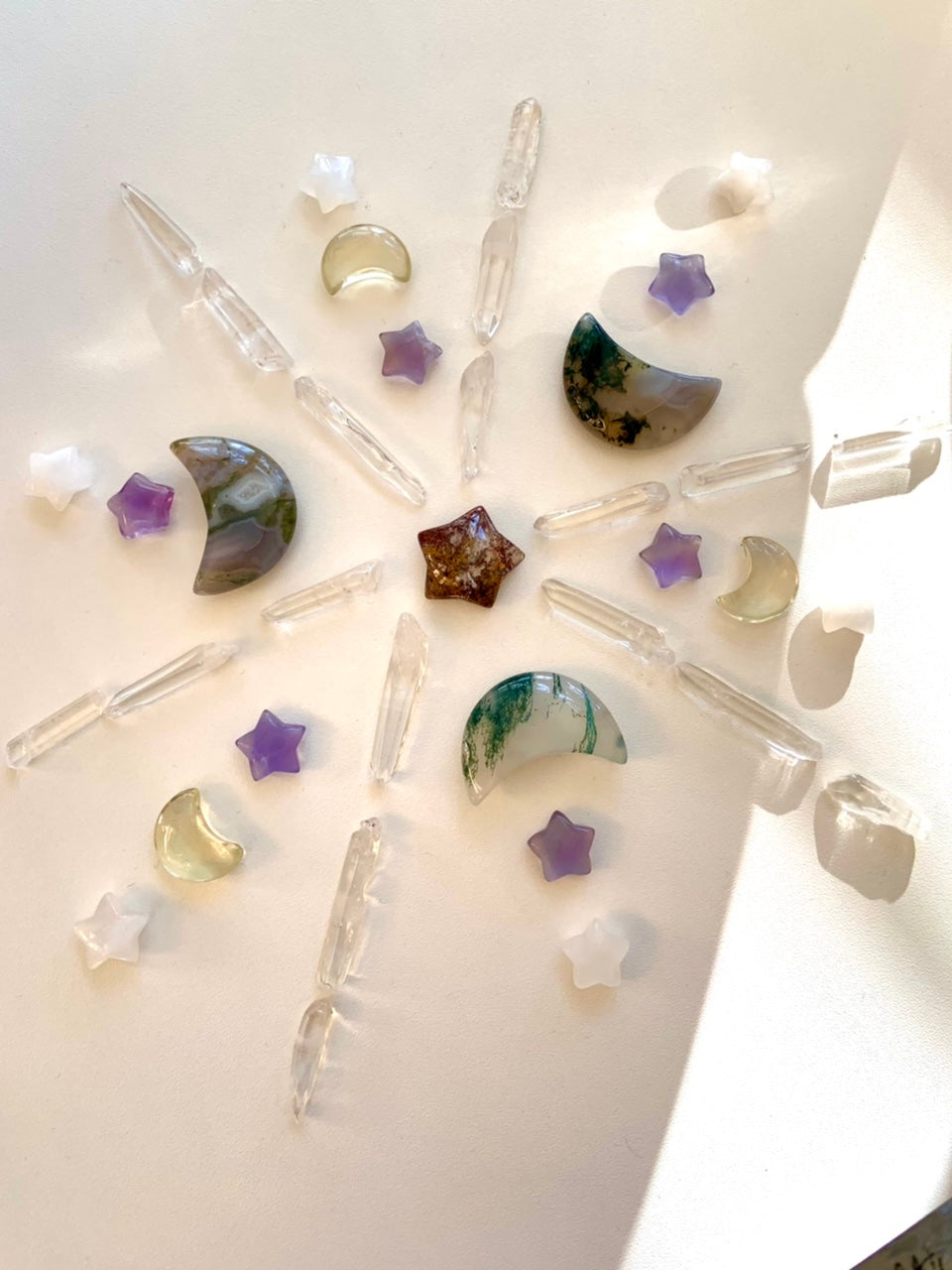 Clear quartz crystal points arranged in inspirational crystal grid with moon and star carvings on white background