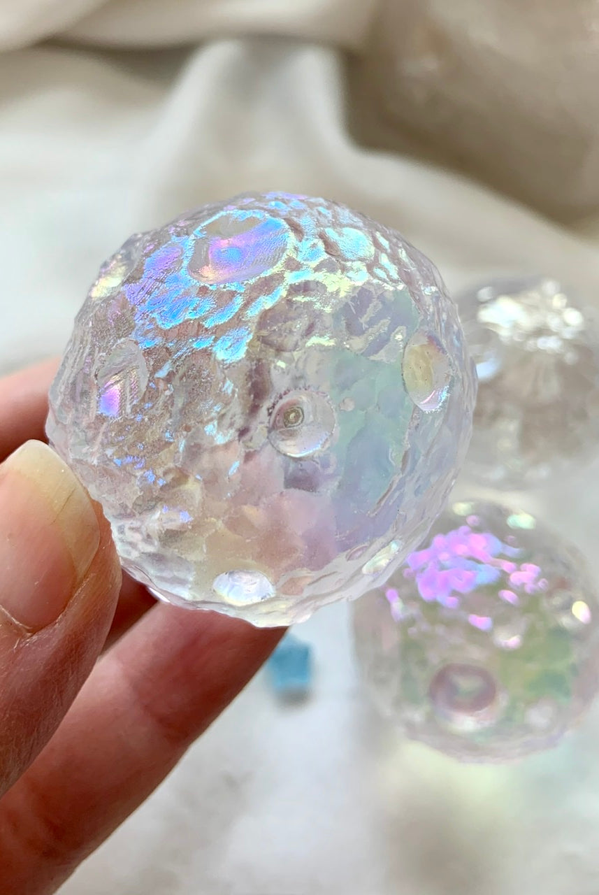 Close-up of Angel Aura Full Moon sphere showing cratered texture & iridescent sheen — a radiant quartz carving inspired by lunar topography.
