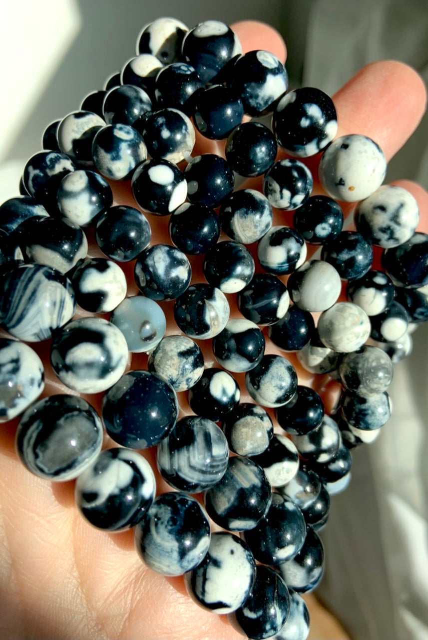 Angled closeup of stacked Orca Agate bracelets in mixed bead sizes, highlighting bold black, white, and gray banded patterns