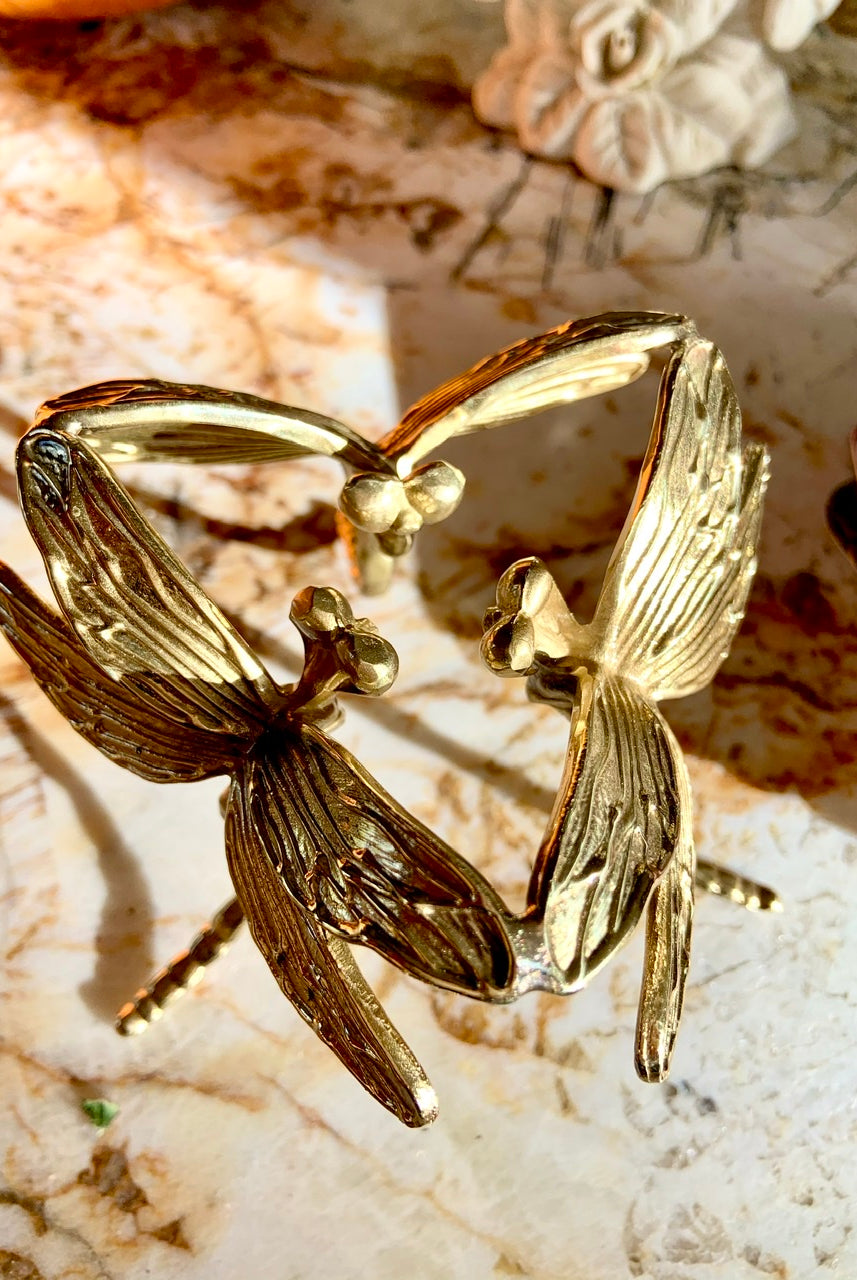 Overhead view of gold dragonfly sphere stand on marble slab — shows intricate wing details of art deco design.