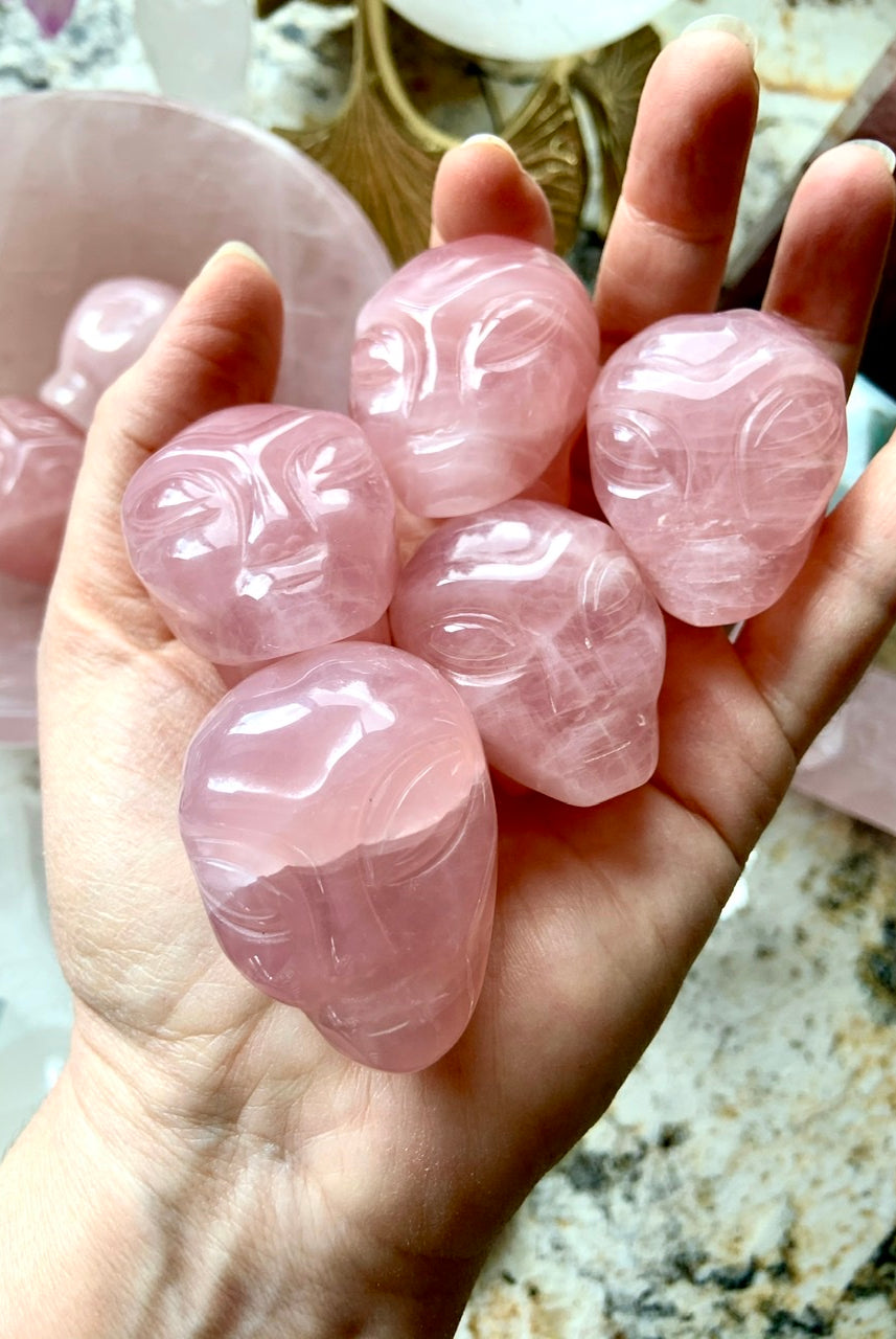 Hand holding five carved Rose Quartz alien heads – crystal carvings for love, heart chakra healing + cosmic energy