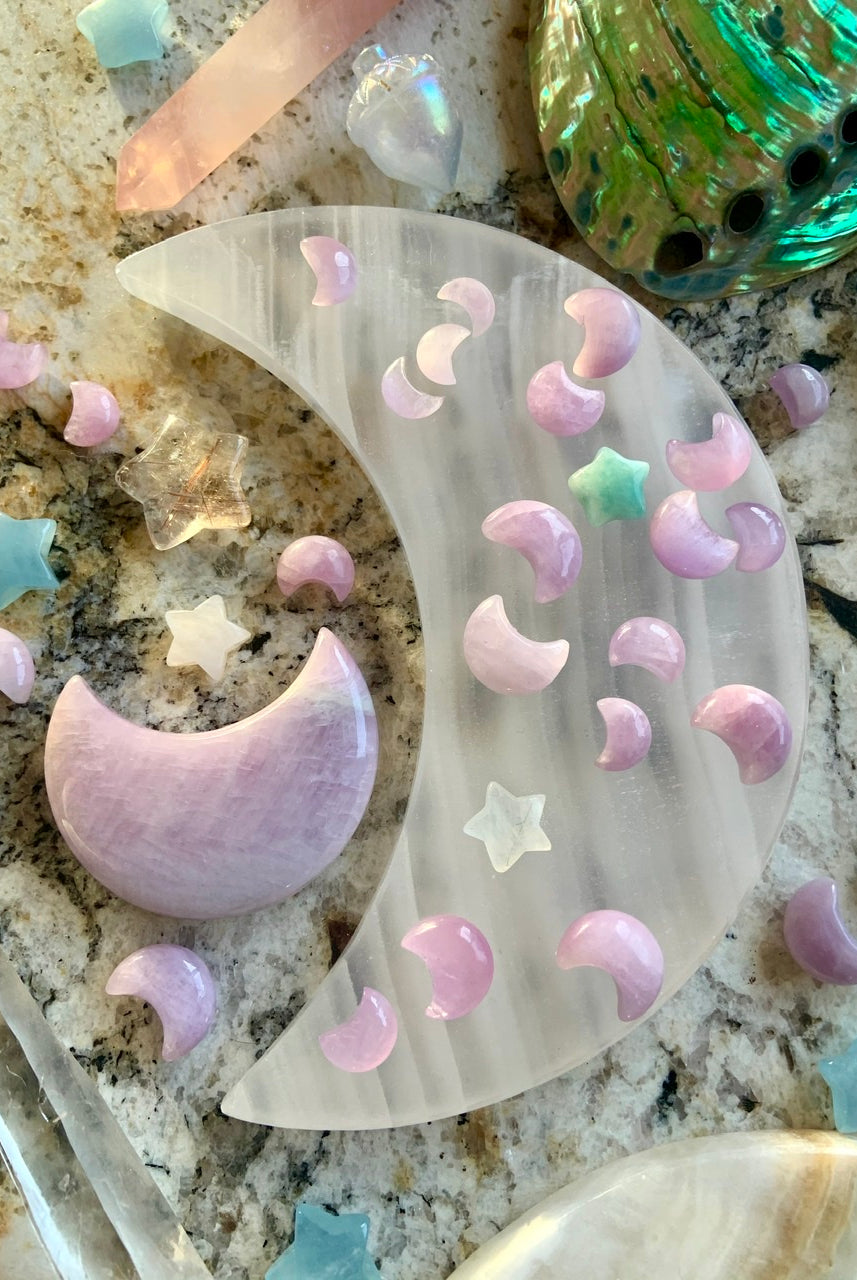 Overhead image of Kunzite moons on a white moon plate with a large Kunzite moon & surrounding crystals — tools for lunar magic & healing intention.