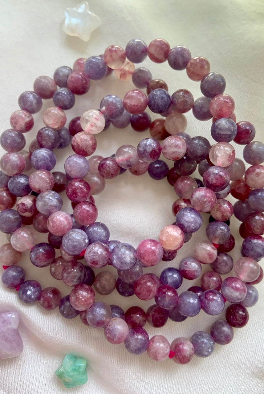 Stack of Unicorn Stone crystal bracelets on white silk — Pink Tourmaline in Lepidolite beaded jewelry with celestial crystals for emotional healing + divine support.