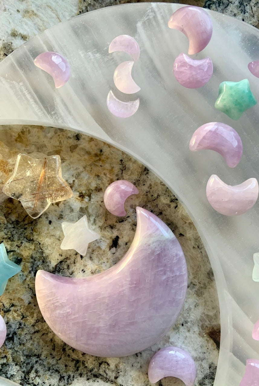 Close-up of Kunzite moons on a white moon plate with large Kunzite moon & crystals — lilac pink crystal carvings for spiritual alignment & self-love.