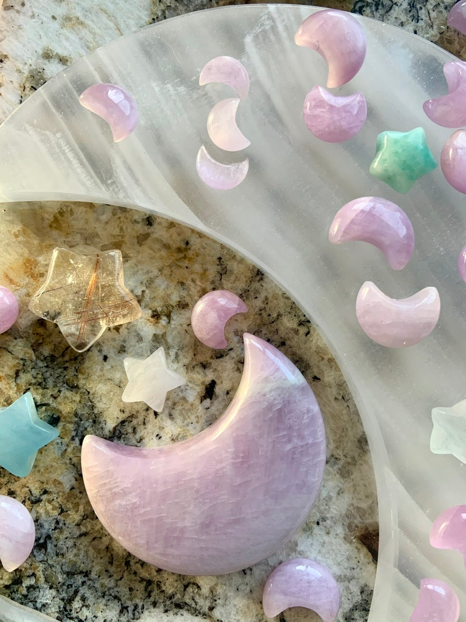 Close-up of Kunzite moons on a white moon plate with large Kunzite moon & crystals — lilac pink crystal carvings for spiritual alignment & self-love.