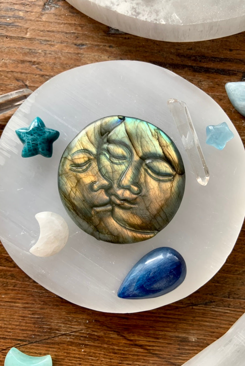 Overhead of labradorite sun and moon carving on round selenite charging plate surrounded by mini crystal stars and moons