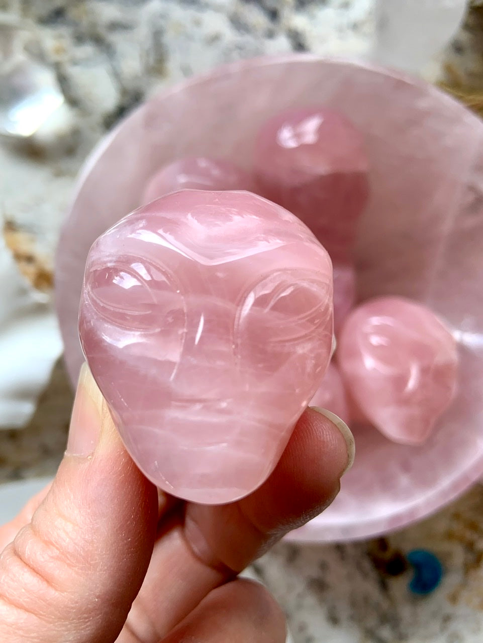 Rose Quartz alien head carving with large eyes and defined brow, shown in a pink crystal bowl on altar