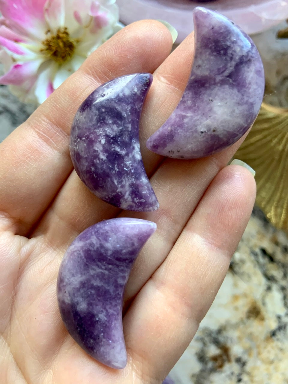 A close up view of our Purple Lepidolite Crescent Moon crystal carvings shown on my hand for scale