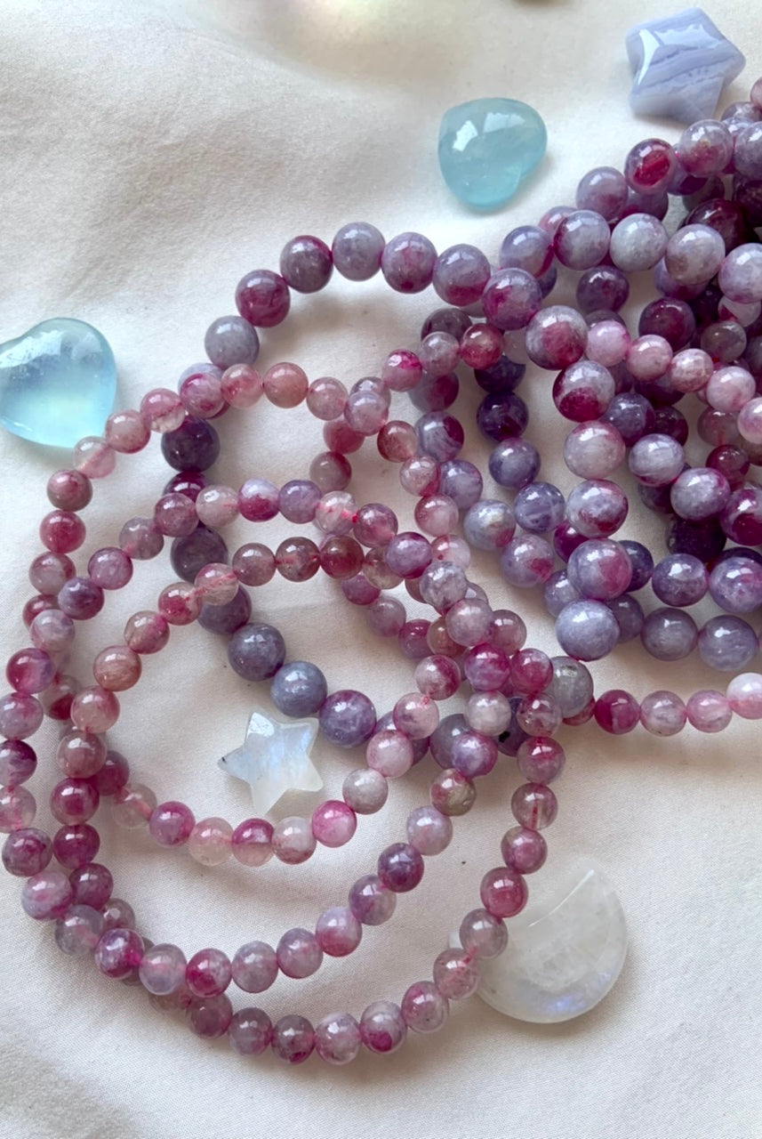 Array of Unicorn Stone bracelets on white silk — assorted beaded sizes shown with Aquamarine hearts + Blue Lace Agate stars for high-vibe crystal gifting.