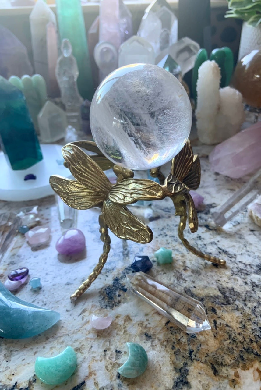 Gold dragonfly sphere stand displaying a clear quartz crystal ball in the midst of a colorful crystal collection.