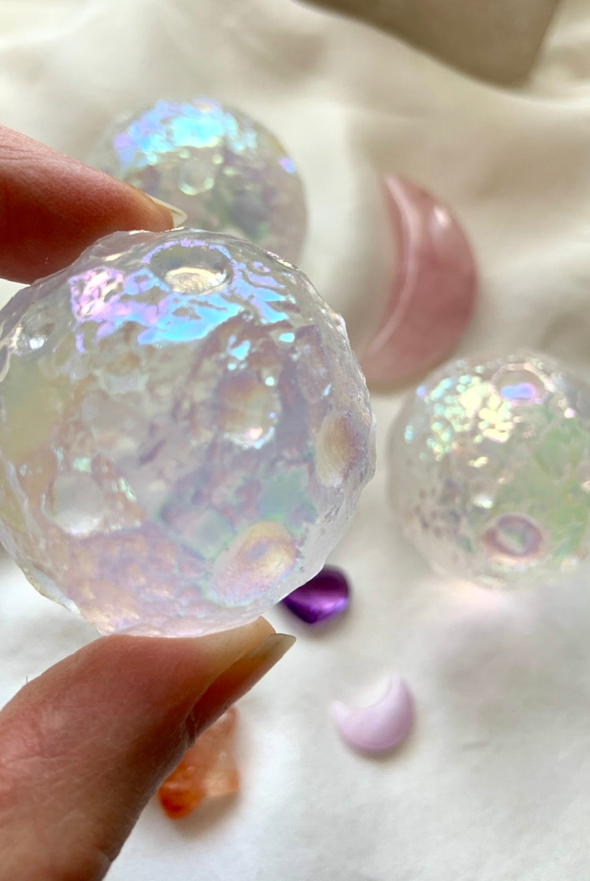 Angled close-up of Angel Aura Quartz moon sphere with surrounding crystals on white silk — celestial carving for divine insight & spiritual energy.