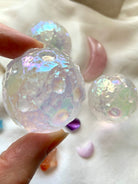 Angled close-up of Angel Aura Quartz moon sphere with surrounding crystals on white silk — celestial carving for divine insight & spiritual energy.