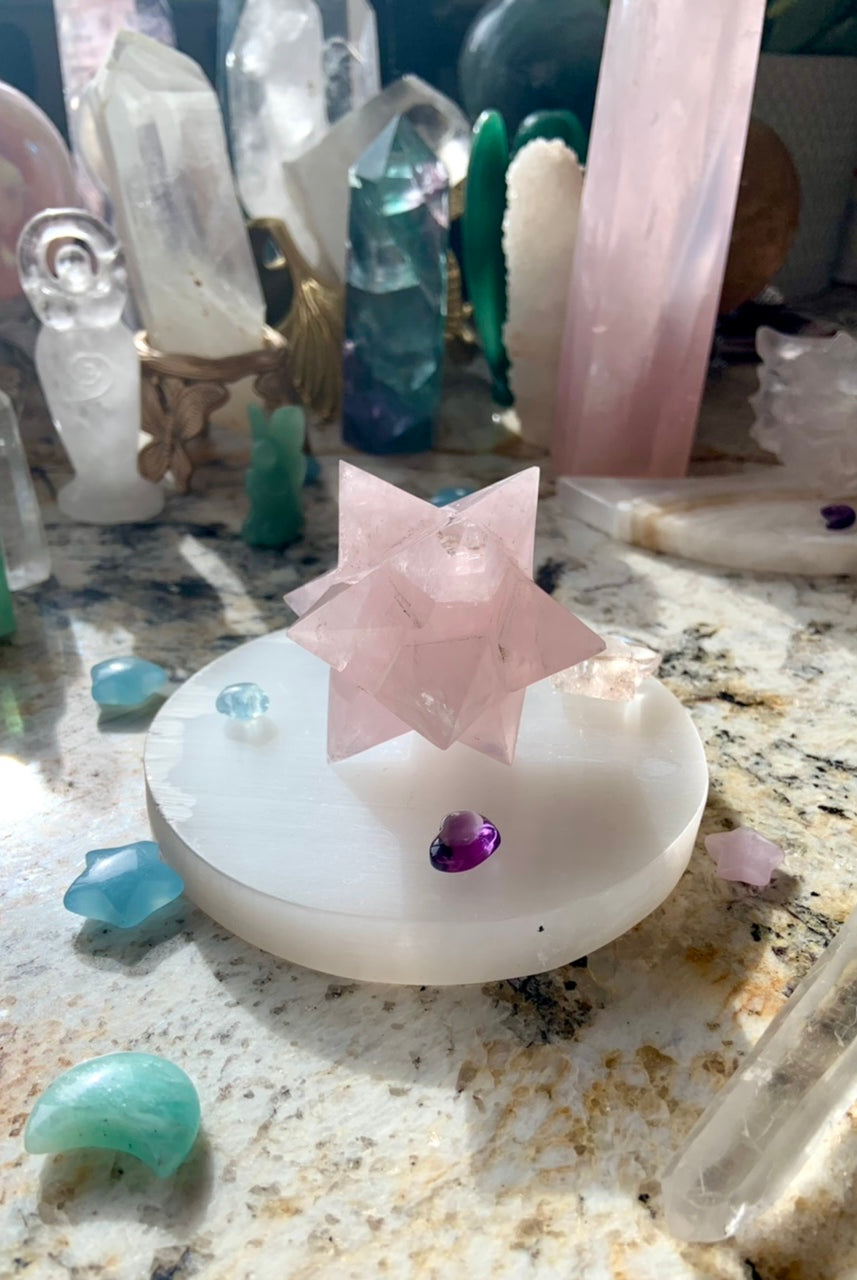 Round selenite plate as a display base for large rose quartz merkaba carving, styled within crystal collection