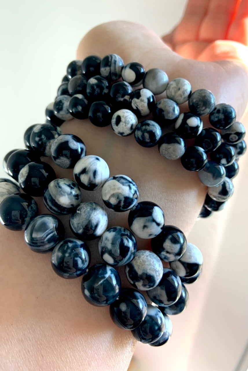 Stack of six Orca Agate bracelets separated into two bead size groups — 10–11mm and 8–9mm — worn on wrist for size comparison