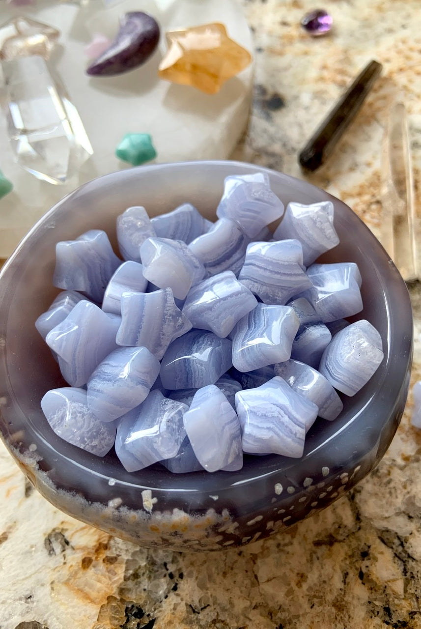 Close-up of Blue Lace Agate stars in an agate bowl with crystal grid in background — serene Throat Chakra stones for sacred space rituals.