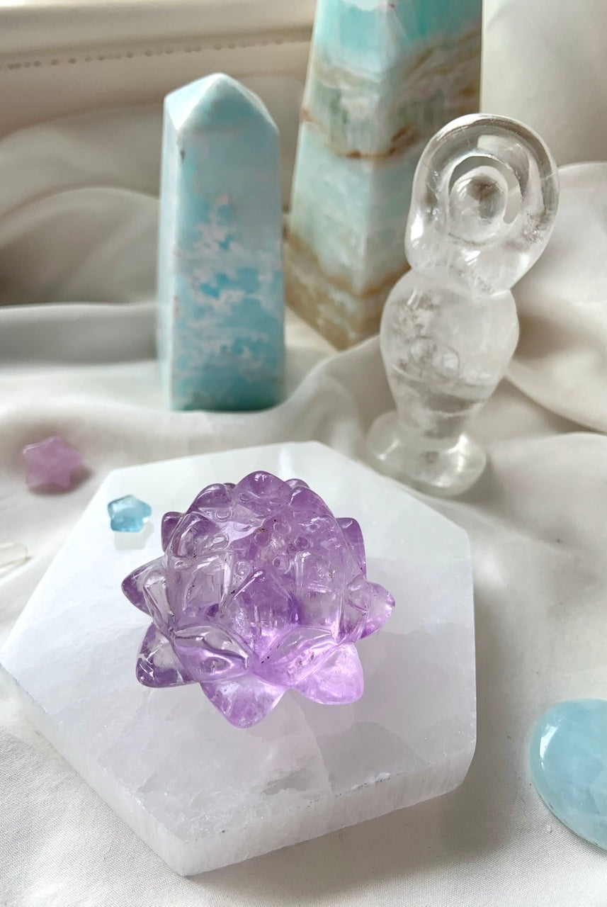 Lifestyle image of a selenite charging plate used as a display base for an amethyst lotus carving, surrounded by crystals