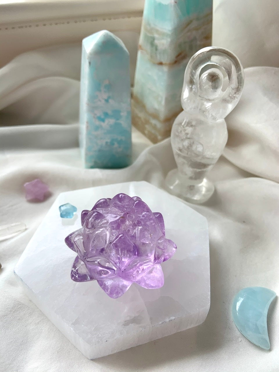 Lifestyle image of a selenite charging plate used as a display base for an amethyst lotus carving, surrounded by crystals