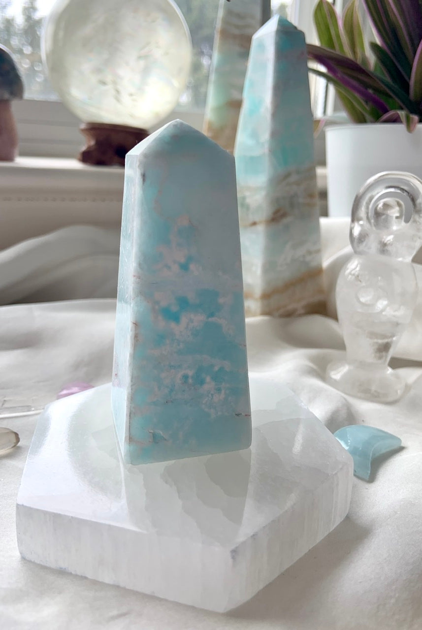 Lifestyle display of selenite hexagon plate holding a Caribbean calcite tower, surrounded by crystals in sacred space décor