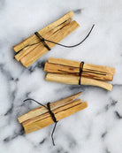 Three Palo Santo bundles tied with black hemp string on white marble background β sacred smudge sticks for energy clearing and spiritual rituals