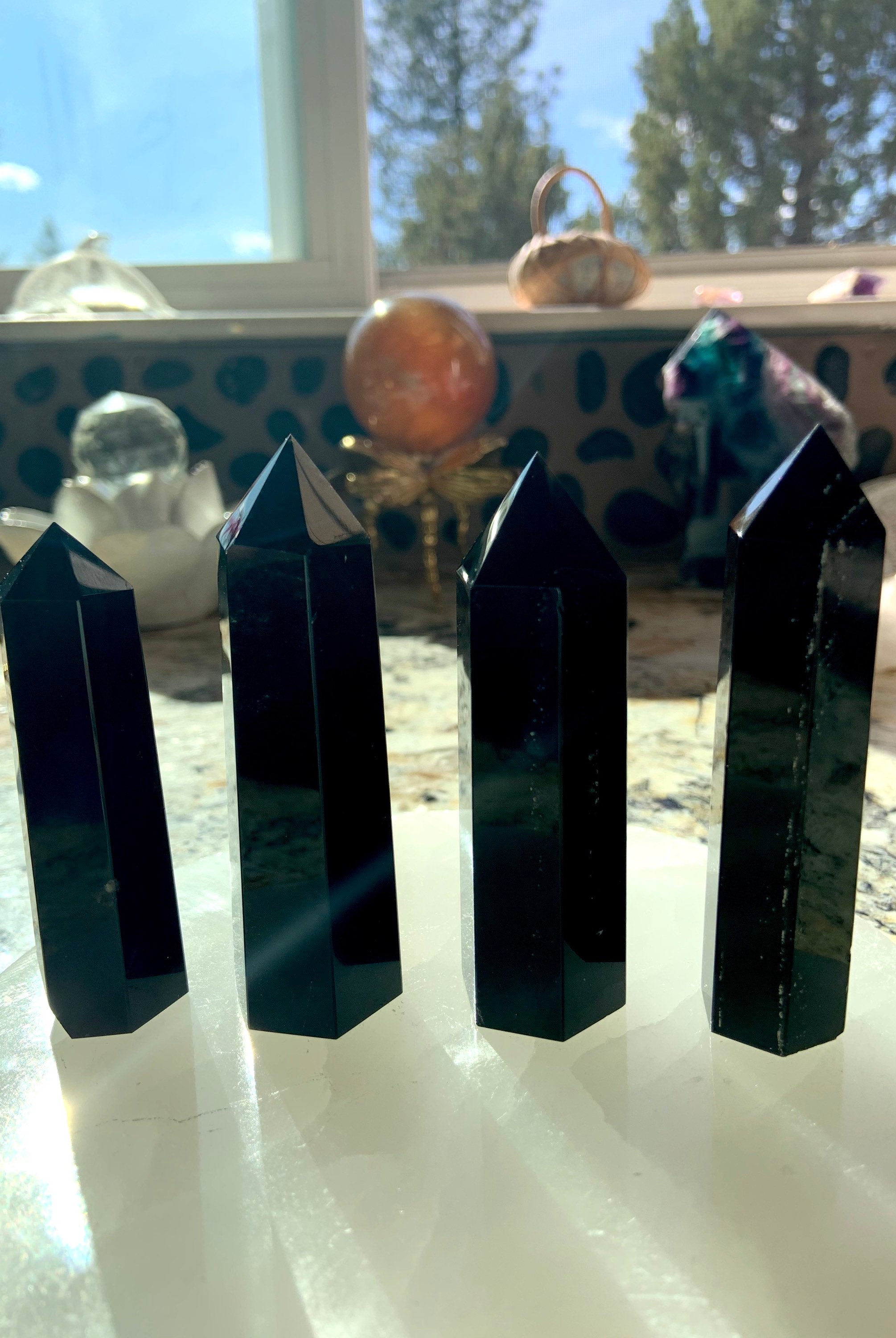An array of black obsidian points shown in a group on top of a selenite plate with crystal spheres in the background. Choose your size from the dropdown menu.