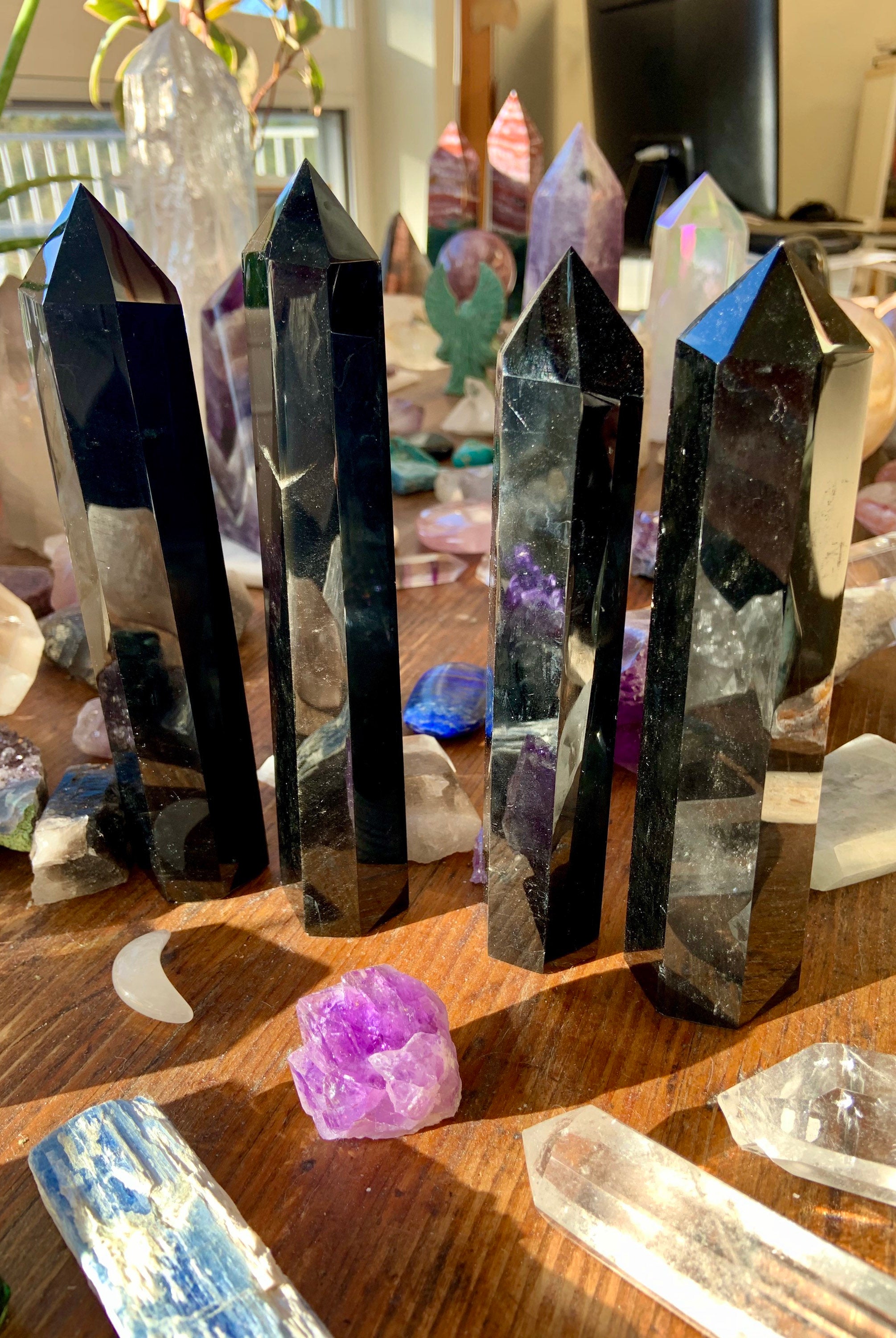 Angled view of four large Black Obsidian towers on a wooden table among a crystal collection — Root Chakra stones for protection & clarity.