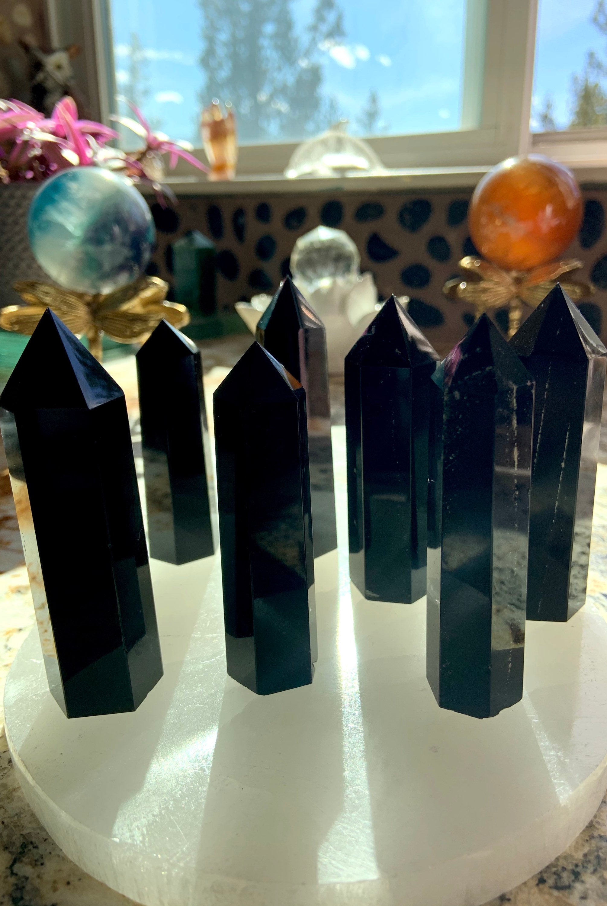 A collection of black obsidian points shown in a group on top of a selenite plate. Choose your size from the dropdown menu.