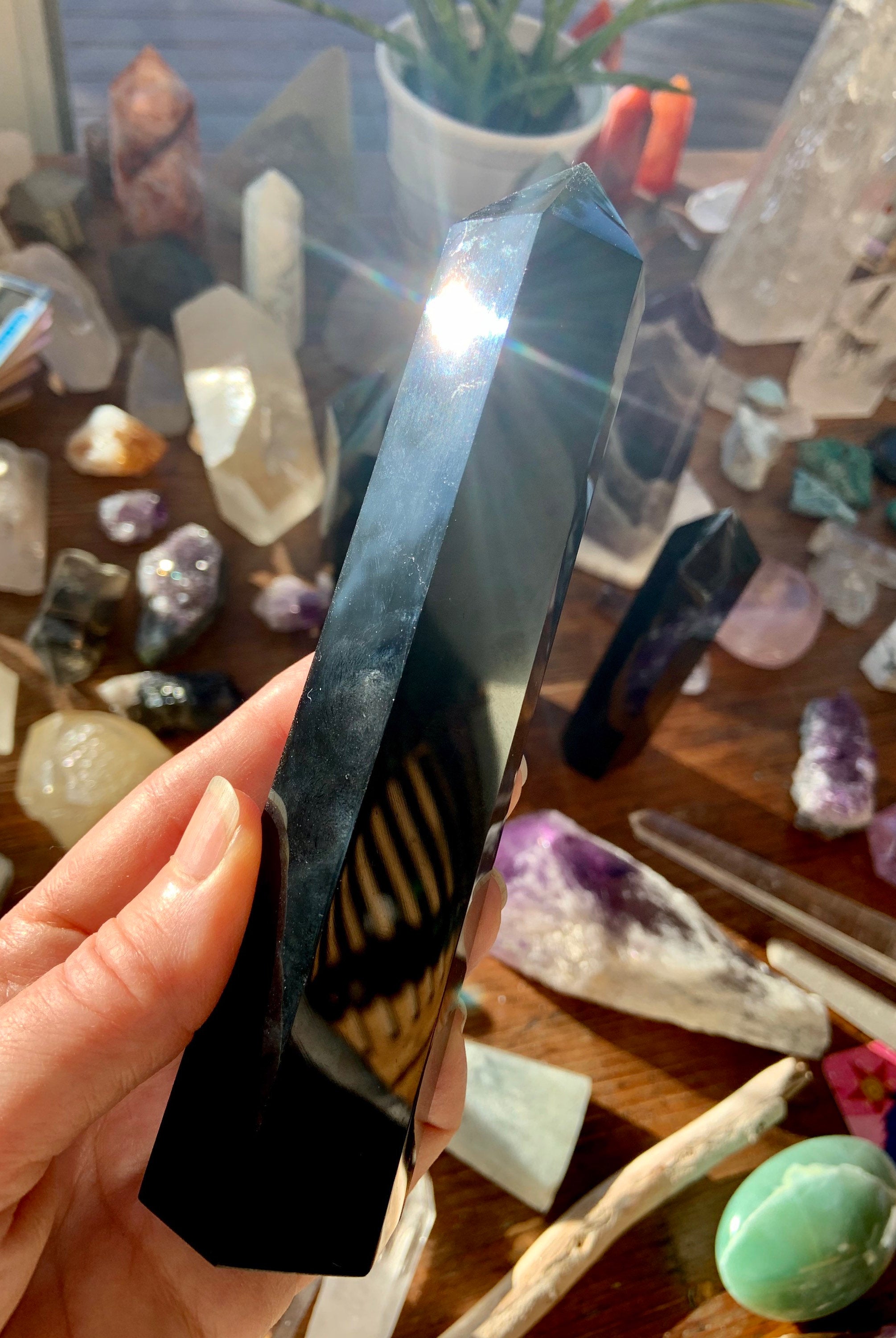 Hand holding large Black Obsidian tower with sunlight glint — polished crystal for spiritual protection & grounding energy.