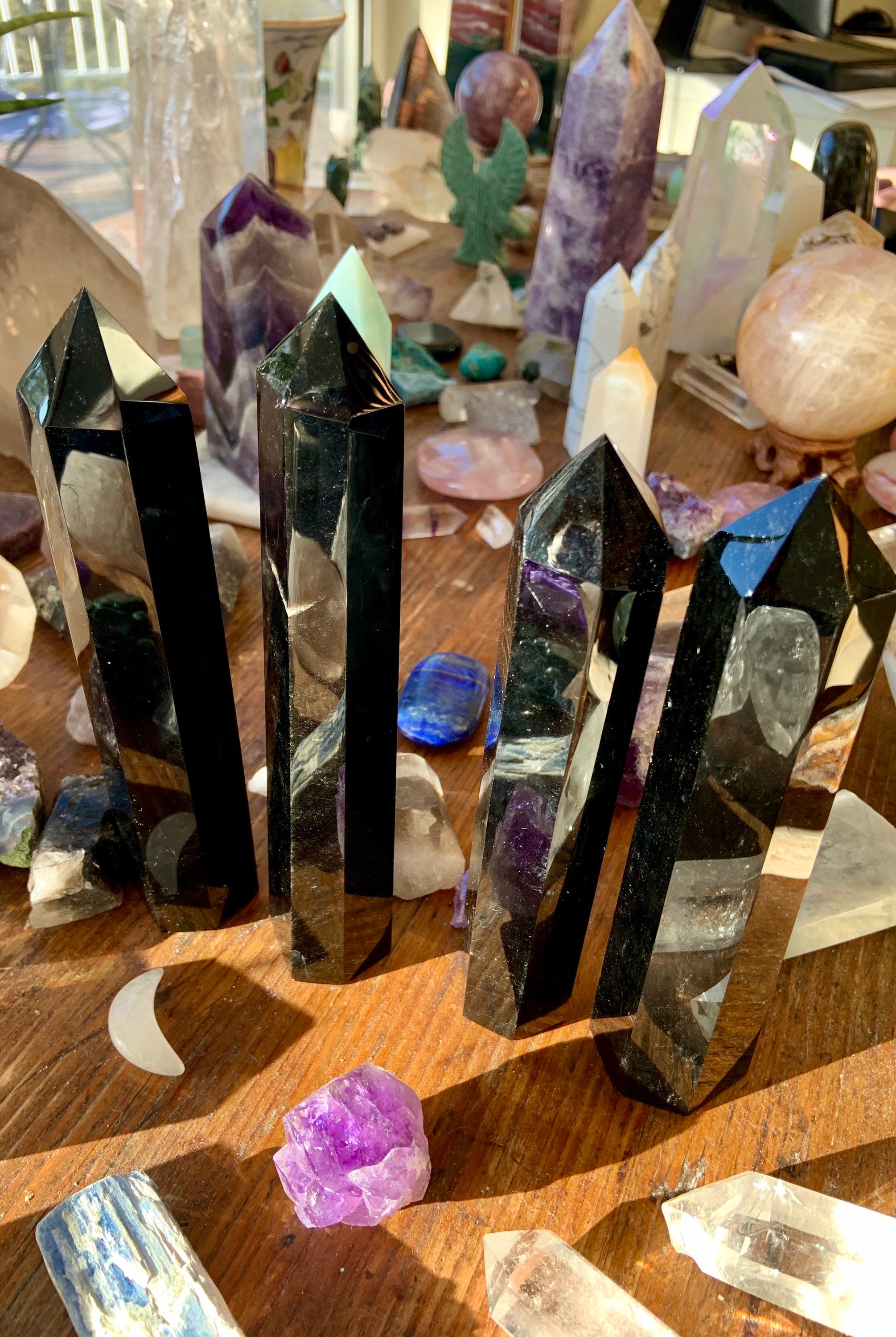 Another angled view of four large Black Obsidian towers on a wooden table with other crystals — grounding stones for energy protection.