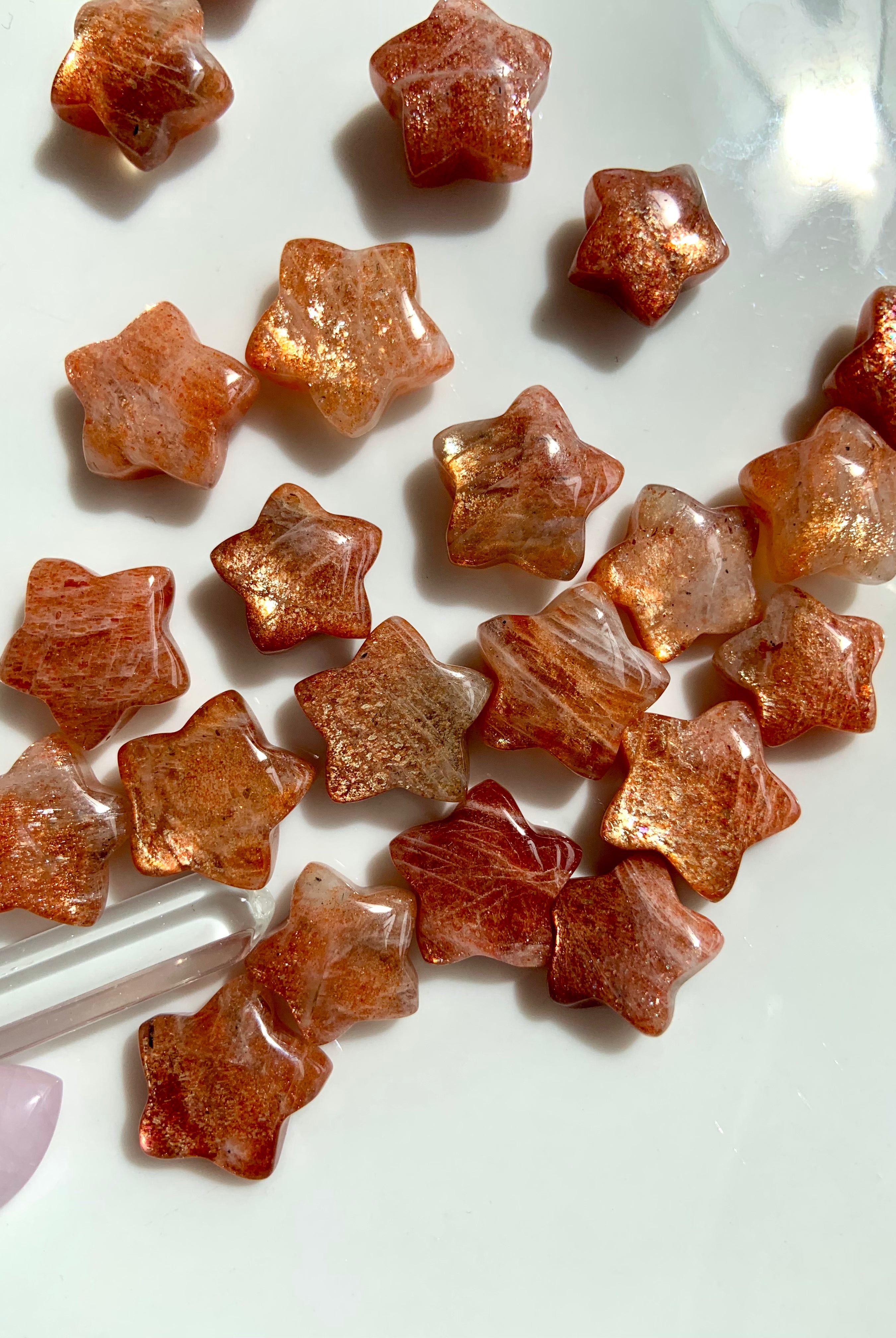 A collection of star-shaped Arusha Sunstone crystals with a golden orange hue and sparkling inclusions, displayed on a white surface.