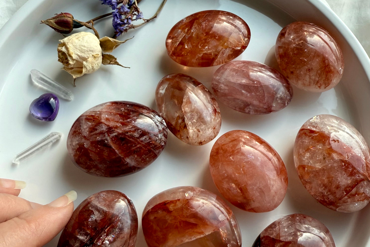Fire Quartz palm stones with deep red hematite inclusions on white plate with amethyst heart and clear quartz points for grounding and healing energy