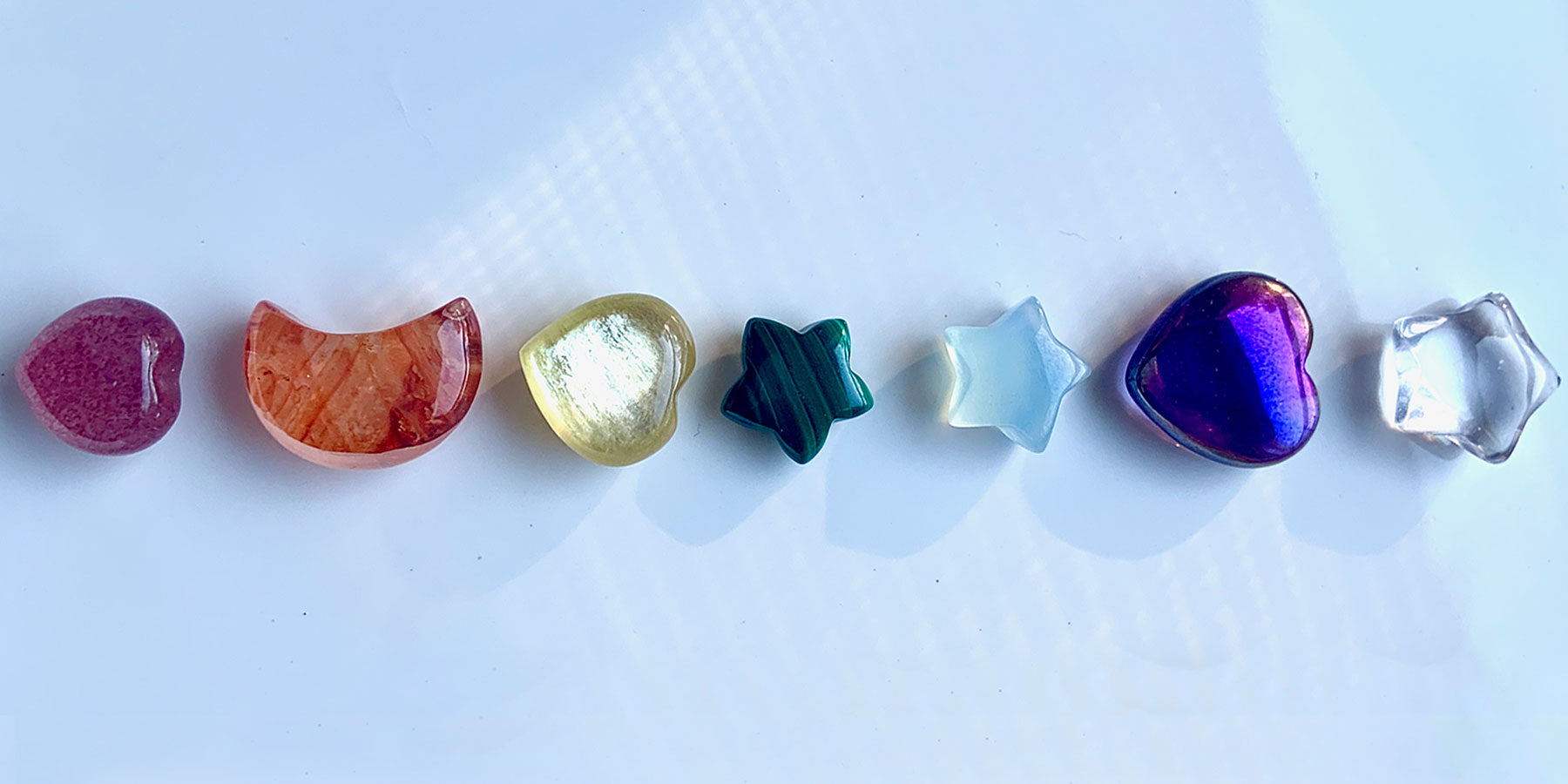 Chakra healing crystals banner featuring 7 mini gemstone carvings — heart, moon, star, and more — symbolizing the seven chakras for balance, alignment, and energy healing.