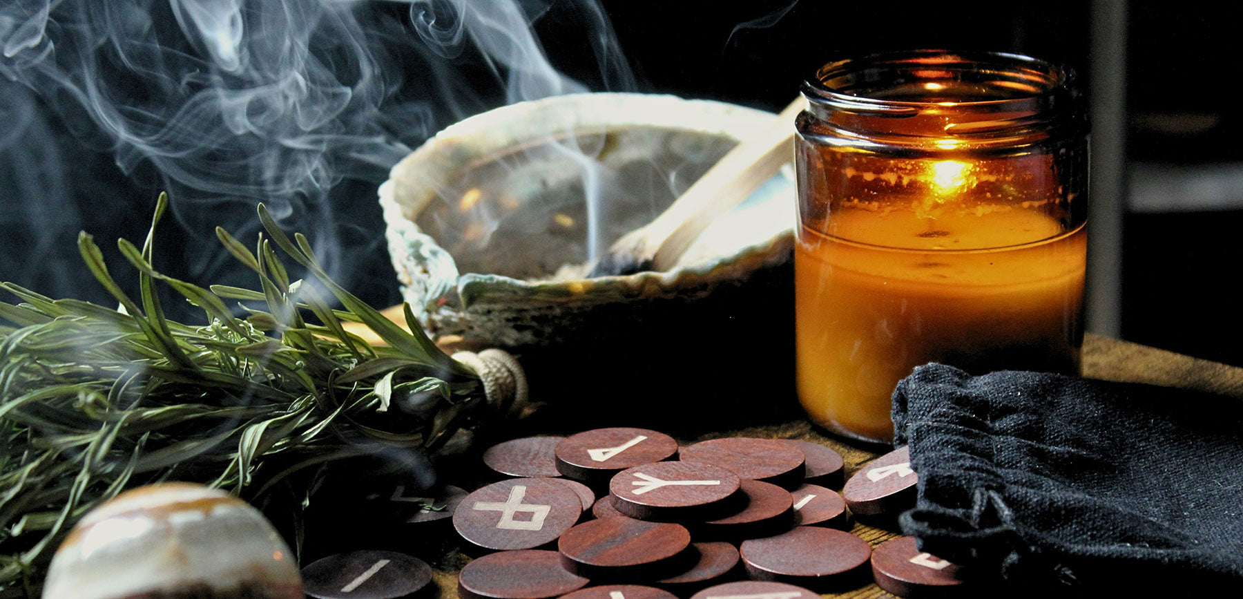 Moody altar scene with burning palo santo in abalone shell, smudge bundle, lit candle, scattered runes, and a crystal ball — a sacred setup for energy clearing, divination, and ritual.