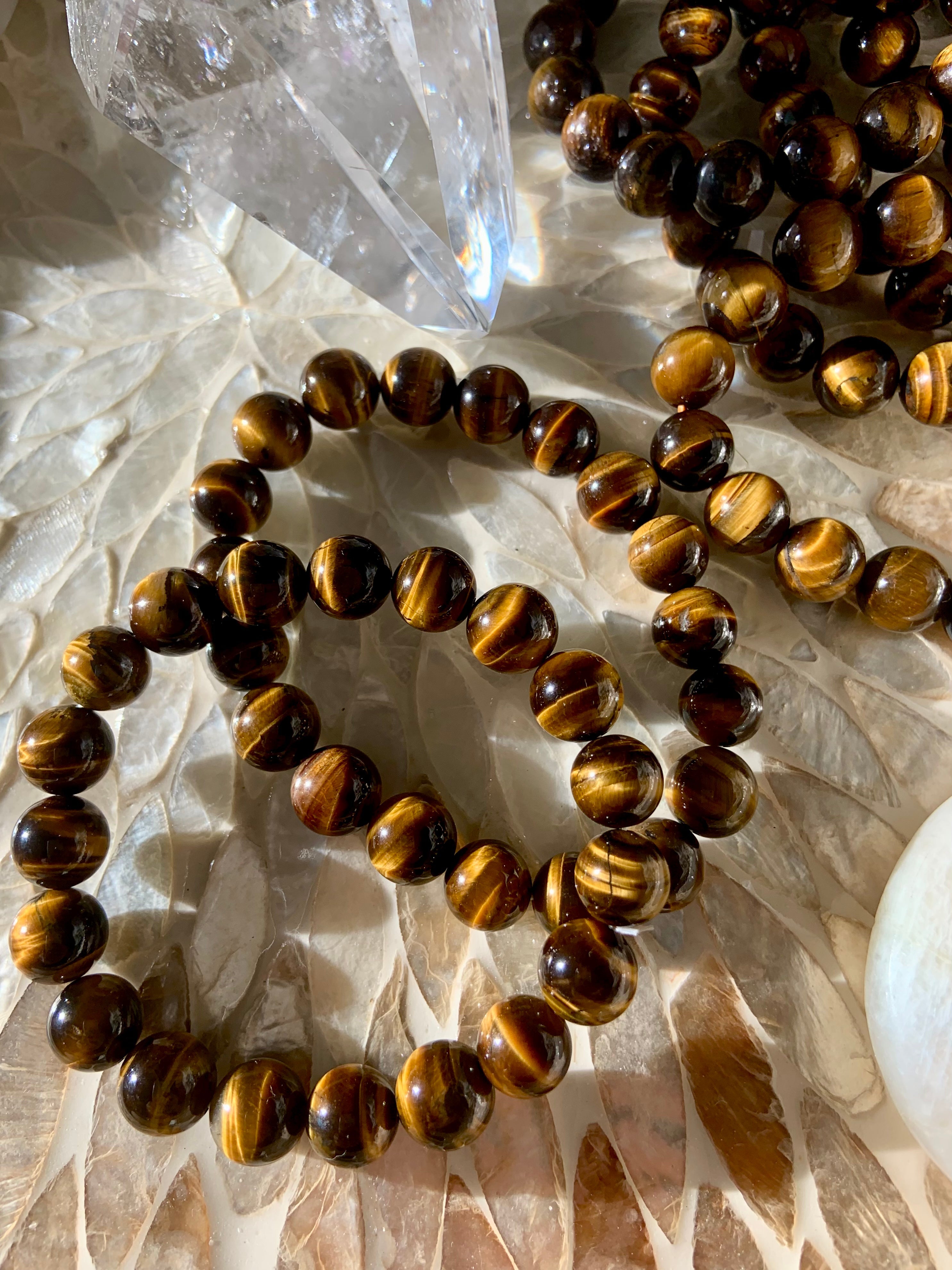 Tiger’s Eye crystals and jewelry displayed on a cream shell inlay tray — golden brown stones with chatoyant bands for confidence, clarity, and protection.