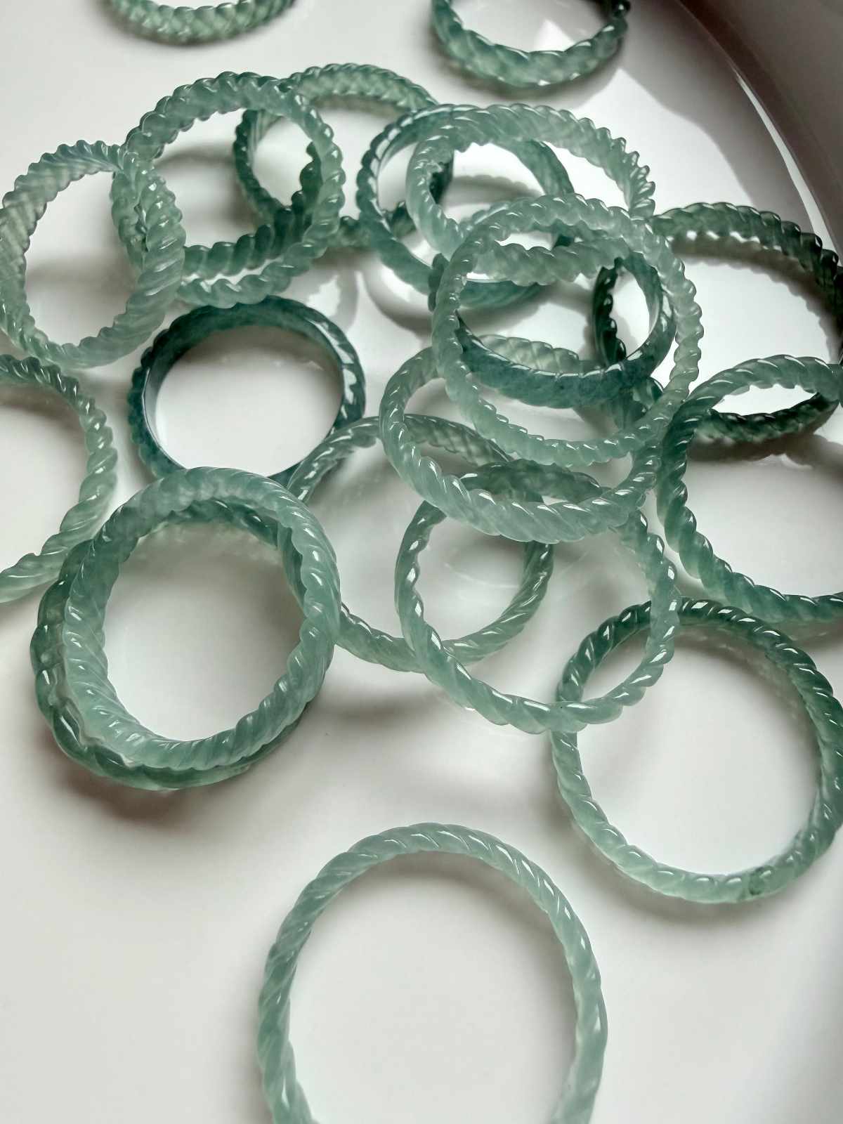 jade jewelry collection featuring blue water jadeite rings with carved and smooth bands in soft green tones on white background