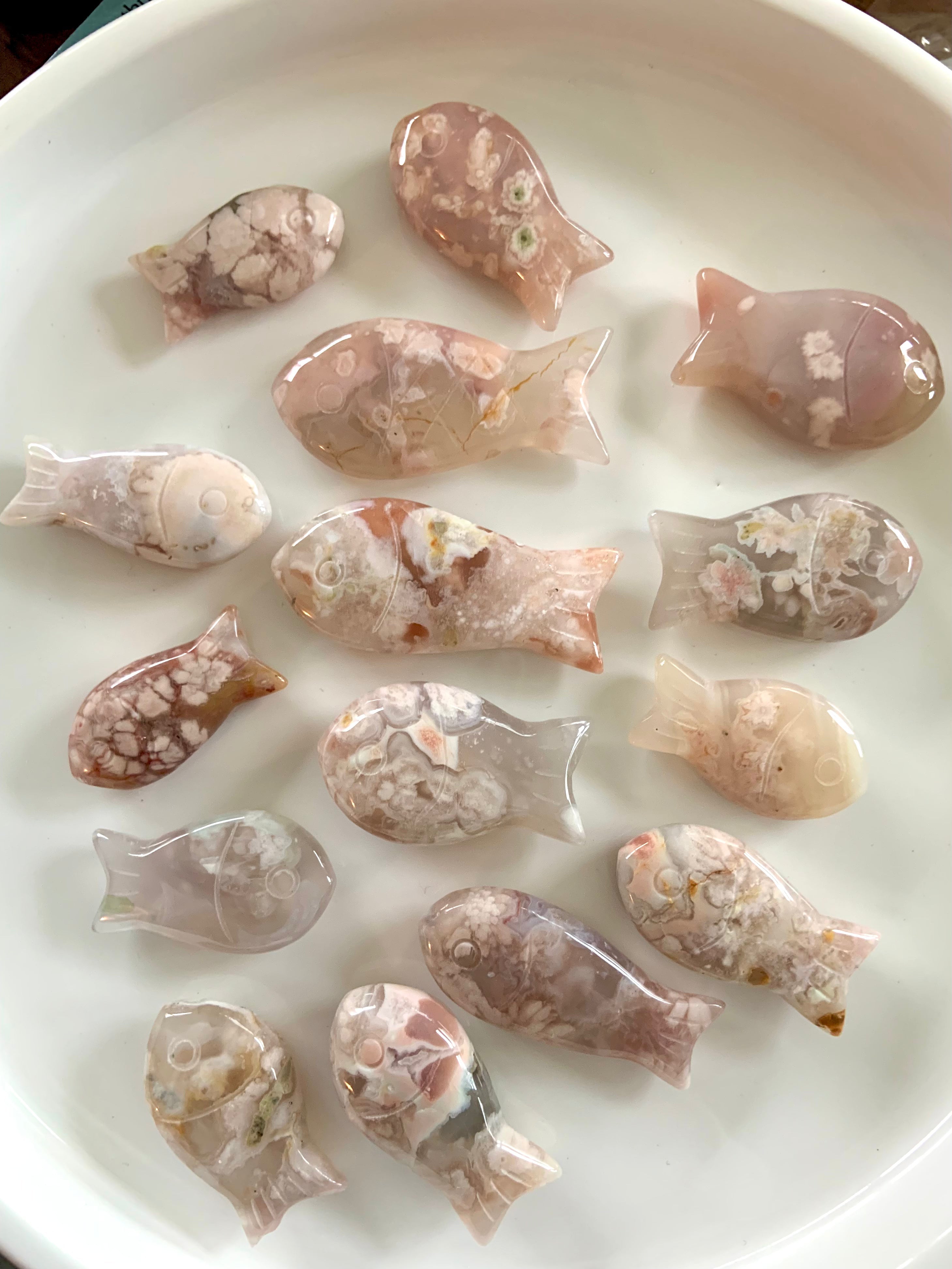 Flatlay of carved crystal animals — unique pastel pink Flower Agate fish carvings arranged like a swimming school.